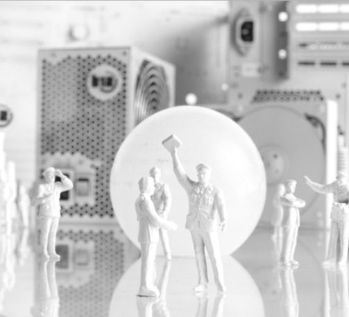 Minimierung von Ausfallzeiten Zwei Miniaturfiguren schütteln sich die Hände vor einem großen weißen Ball und technischen Geräten.