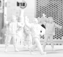 IT-Werkstatt Vier weiße Figuren interagieren mit einem großen Bauwerk, umgeben von kleinen Metallteilen.